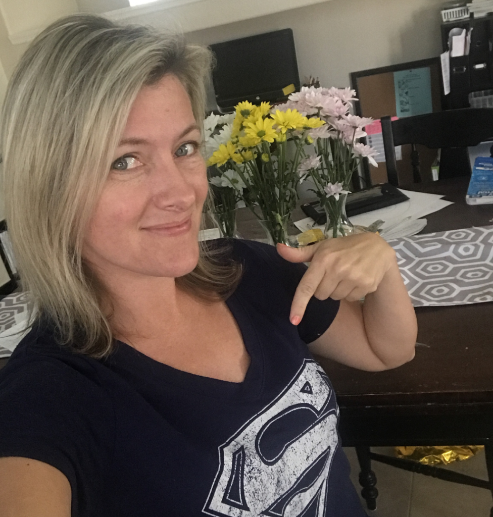 Blond woman wearing a navy superman shirt and pointing to the S